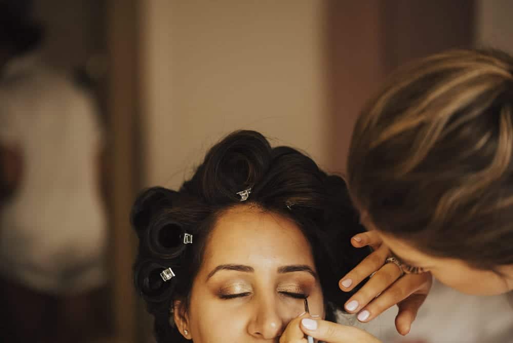close up of makeup artist applying indivual eyelashes to bridesmaid with hair rollers