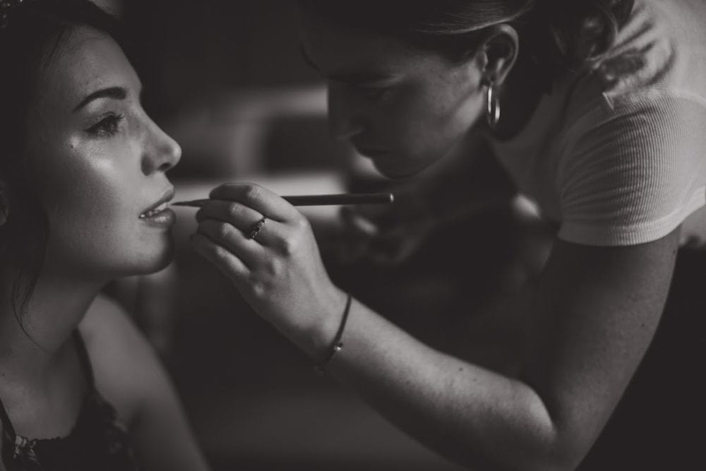 close up of makeup artist applying lipstick to bride with glowing makeup