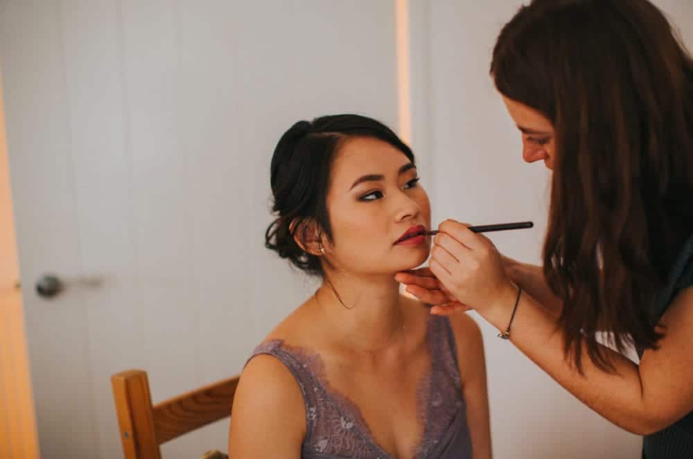 makeup artist applying lipstick to bridesmaid
