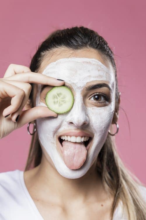 woman holding cucumber wearing facemask against pink background